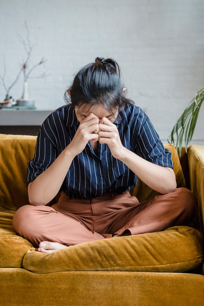 Woman sitting on a couch with hands on face, expressing stress in a modern living room setting.